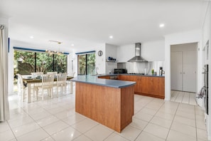 Een moderne keuken met een centraal eiland, een eethoek met tafel en stoelen, en uitzicht op groen.