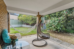 Een terras met een hangstoel, een glazen tafel met een vaas en een bakstenen muur.