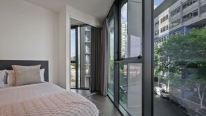 A modern bedroom with a large bed, a view of the city through floor-to-ceiling windows, and a sliding glass door leading to an outdoor area.