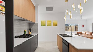 A modern kitchen with grey cabinets, a white countertop, and a built-in dishwasher. There are three yellow wall art pieces and a ceiling fan.