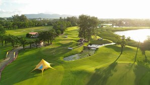 Un campo de golf con una carpa, elementos de agua y un lago al fondo.