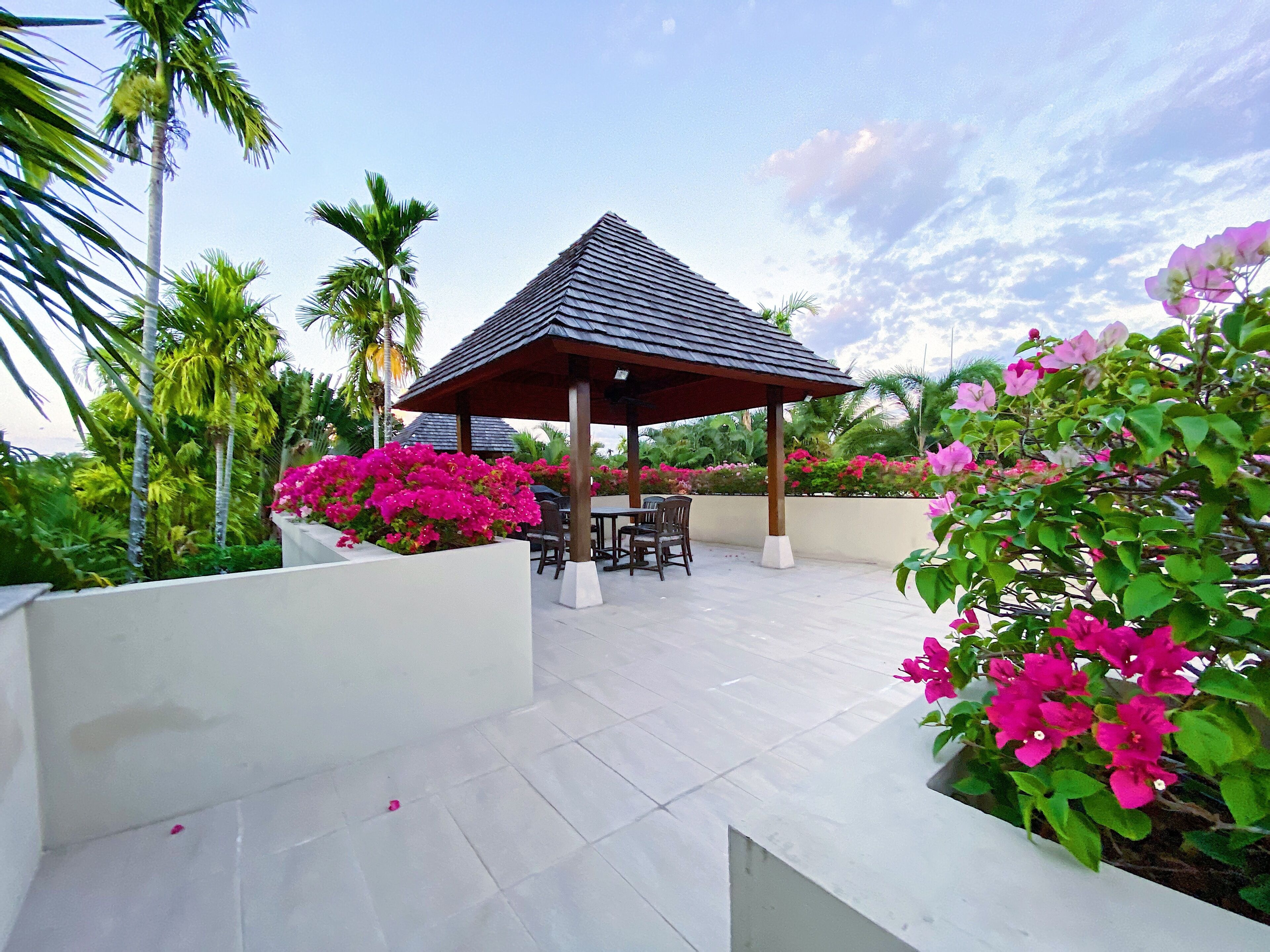 A covered outdoor seating area with a gazebo, surrounded by lush greenery and flowering plants.