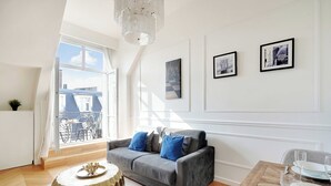 A modern living room with a grey sofa, a round wooden coffee table, and a dining area with a wooden table and white plates. - Magnificent Apartment -1br-4p- Champs-elysees (Paris)