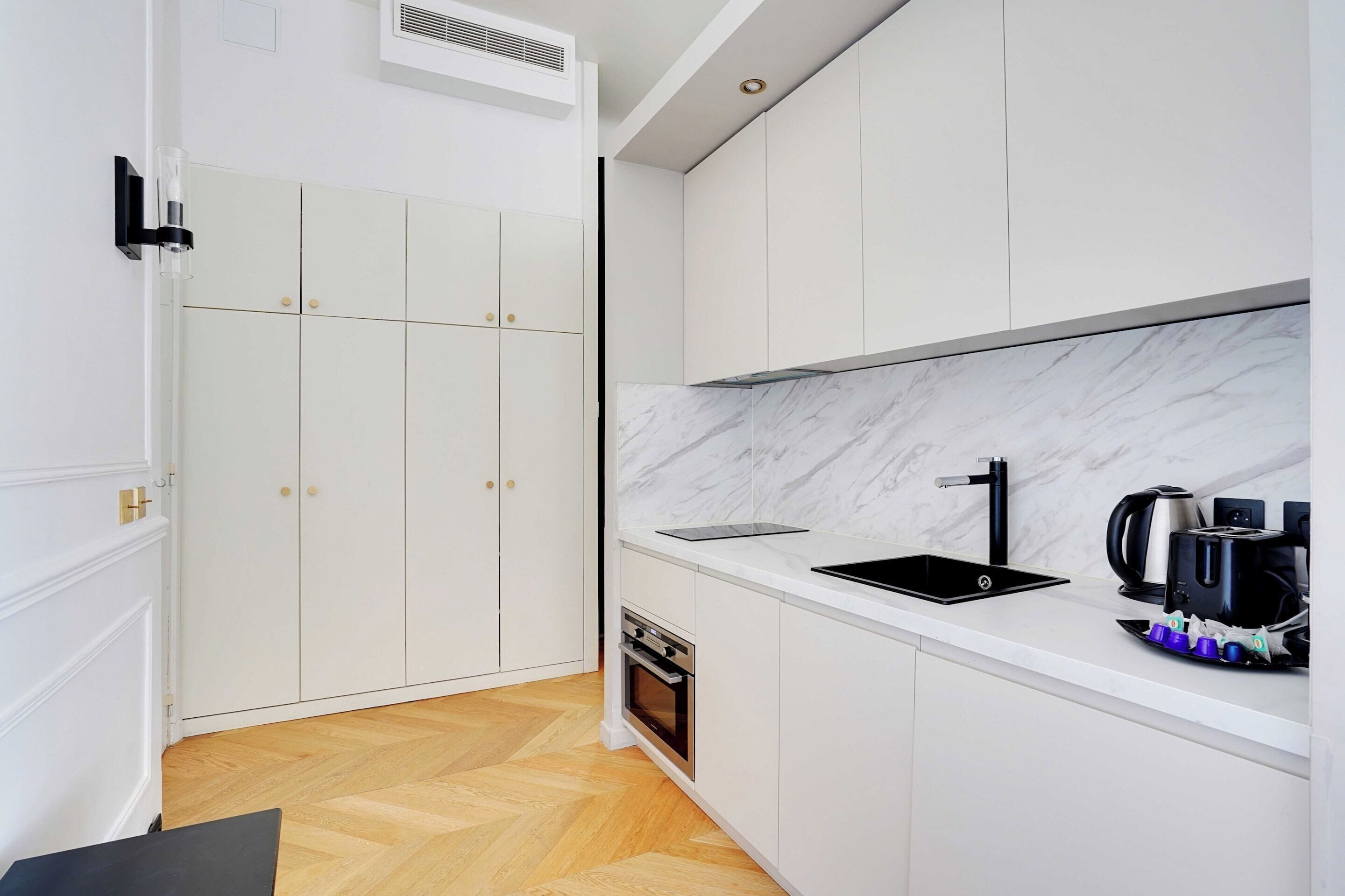 A modern kitchen with white cabinetry, a marble backsplash, a black sink, and a built-in oven.