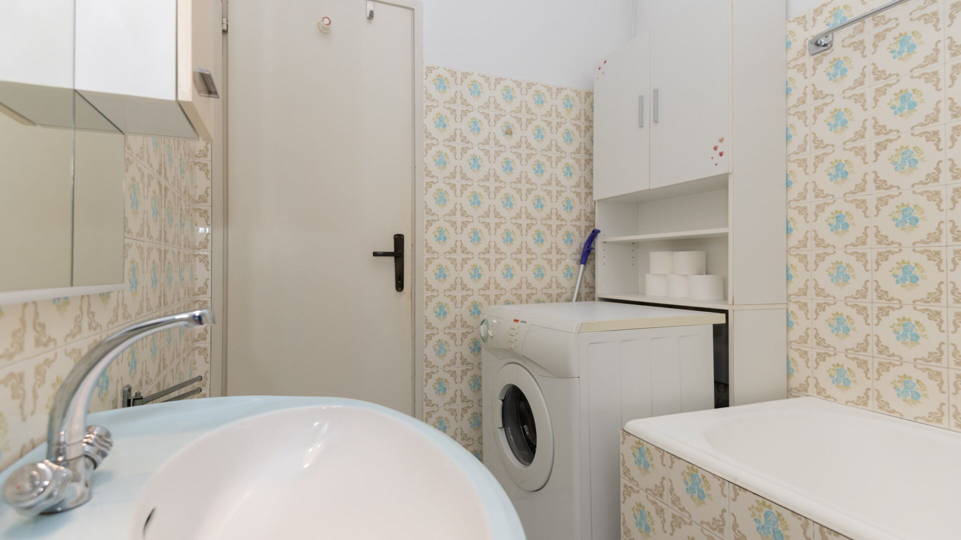 Een badkamer met een wastafel, een wasmachine en behang met een patroon.