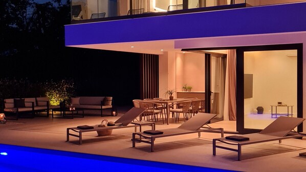 A modern outdoor living area with a pool, lounge chairs, and a dining table.
