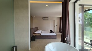 A modern hotel room with a large bed, a separate bathroom, and a balcony with a view.