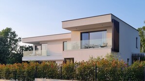 Una casa moderna de dos pisos amb un balcó, grans finestres i un terrat pla.