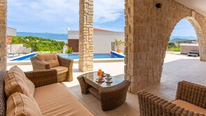 Eine Terrasse mit Korbmöbeln, einem Glastisch und einem Pool.