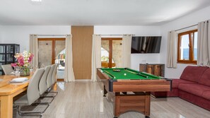Ein Billardtisch in einem Raum mit Essbereich, einer Couch und einem Fernseher an der Wand.