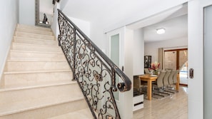 Eine Treppe mit aufwendig gestalteten schwarzen Metallgeländern, ein Esstisch mit Stühlen und eine weiße Tür.