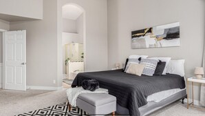 A bedroom with a bed, a bedside table, a lamp, a mirror, and a door.