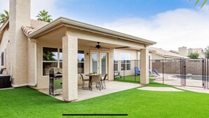 A covered patio area with a grill, outdoor seating, and a pool.