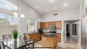 A modern kitchen with a central island, wooden cabinets, stainless steel appliances, and a large window providing natural light.