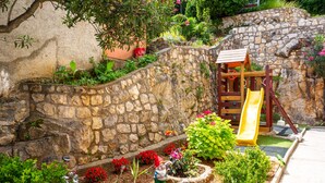 A stone wall, a wooden slide, and a garden with flowers and plants. - Apartman Zora 3 by Villas guide (Mošcenice)