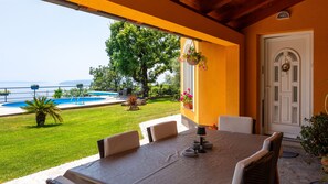 A covered outdoor dining area with a pool, chairs, and a table.