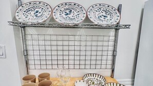A kitchen area with a metal rack holding plates and bowls, a wooden table with mugs and a wine glass, and a metal rack with black pans. - 3-bedroom apartment in charming Philadelphia with WiFi, AC (Philadelphia)