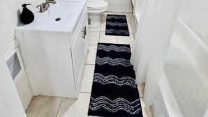 A compact bathroom with a white sink, toilet, and bathtub. There are two black and white patterned rugs on the floor. - 3-bedroom apartment in charming Philadelphia with WiFi, AC (Philadelphia)