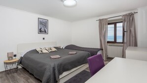A bedroom with two beds, a bedside table, a lamp, a framed picture on the wall, and a window with curtains.