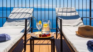 Two lounge chairs with white cushions, a wooden table with a pitcher of water, strawberries, and a glass of drink, and a straw hat on the right.