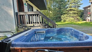 A hot tub with a wooden deck and a staircase leading to a house.