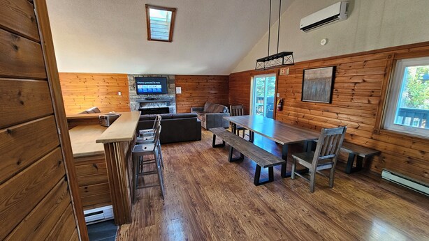 A cozy cabin-style interior with a wooden dining table, benches, and a television mounted on the wall.