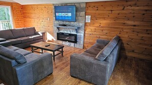 A cozy living room with a stone fireplace, wooden walls, and grey sofas.