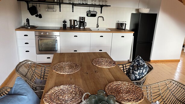 Una cucina moderna con mobili bianchi, un tavolo da pranzo in legno con sottopiatti intrecciati e un frigorifero nero.