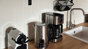 Una cucina con macchina del caffè, bollitore e macchina per espresso. È presente un lavello e uno scaffale con bicchieri.
