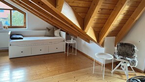 Una camera da letto mansardata con tetto spiovente, travi in legno, un divano bianco, un tavolino rotondo e una poltrona in velluto.