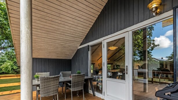 A covered outdoor patio with a table and chairs, a grill, and a view into the house.