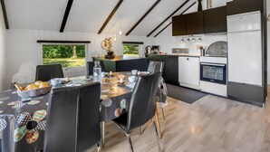 A modern kitchen with a dining area, featuring a large island, built-in appliances, and a view of greenery outside.