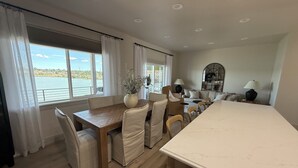 Un comedor con mesa y sillas de madera, un jarrón con flores y vista al agua.