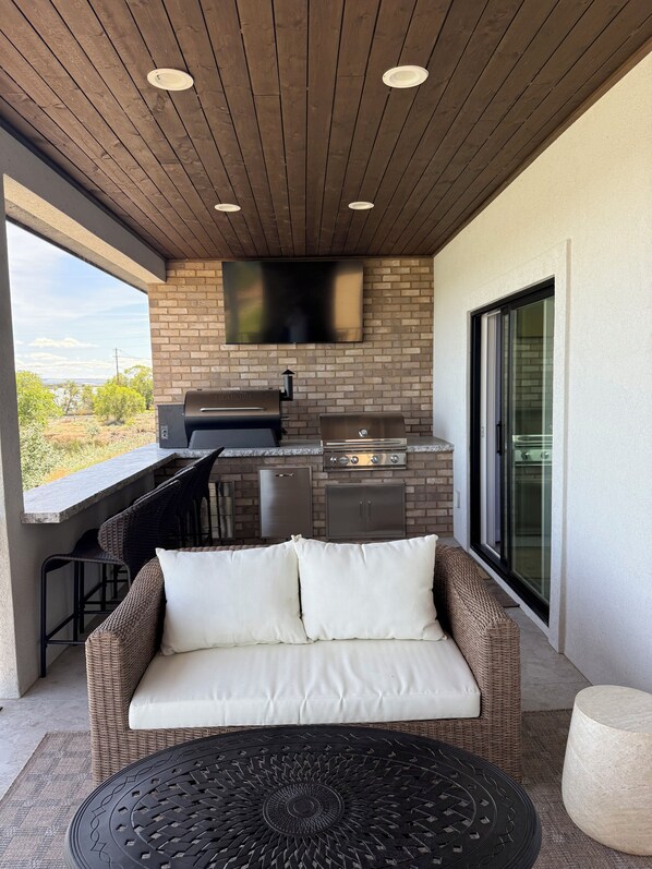 Un patio al aire libre con una parrilla, un televisor de pantalla plana, muebles de mimbre y vistas al paisaje.