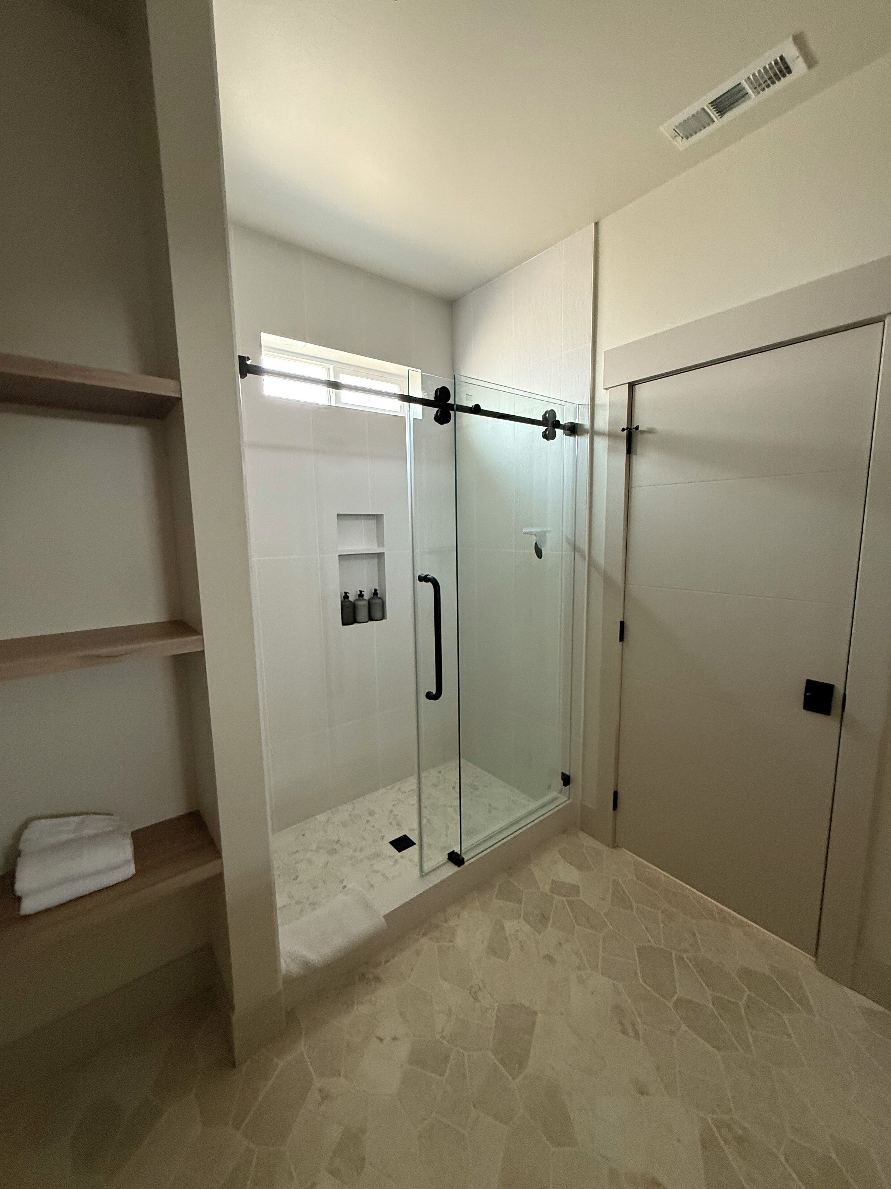 Ein modernes Badezimmer mit einer Duschkabine aus Glas, einer integrierten Ablage mit Pflegeprodukten und einem geräumigen begehbaren Kleiderschrank.