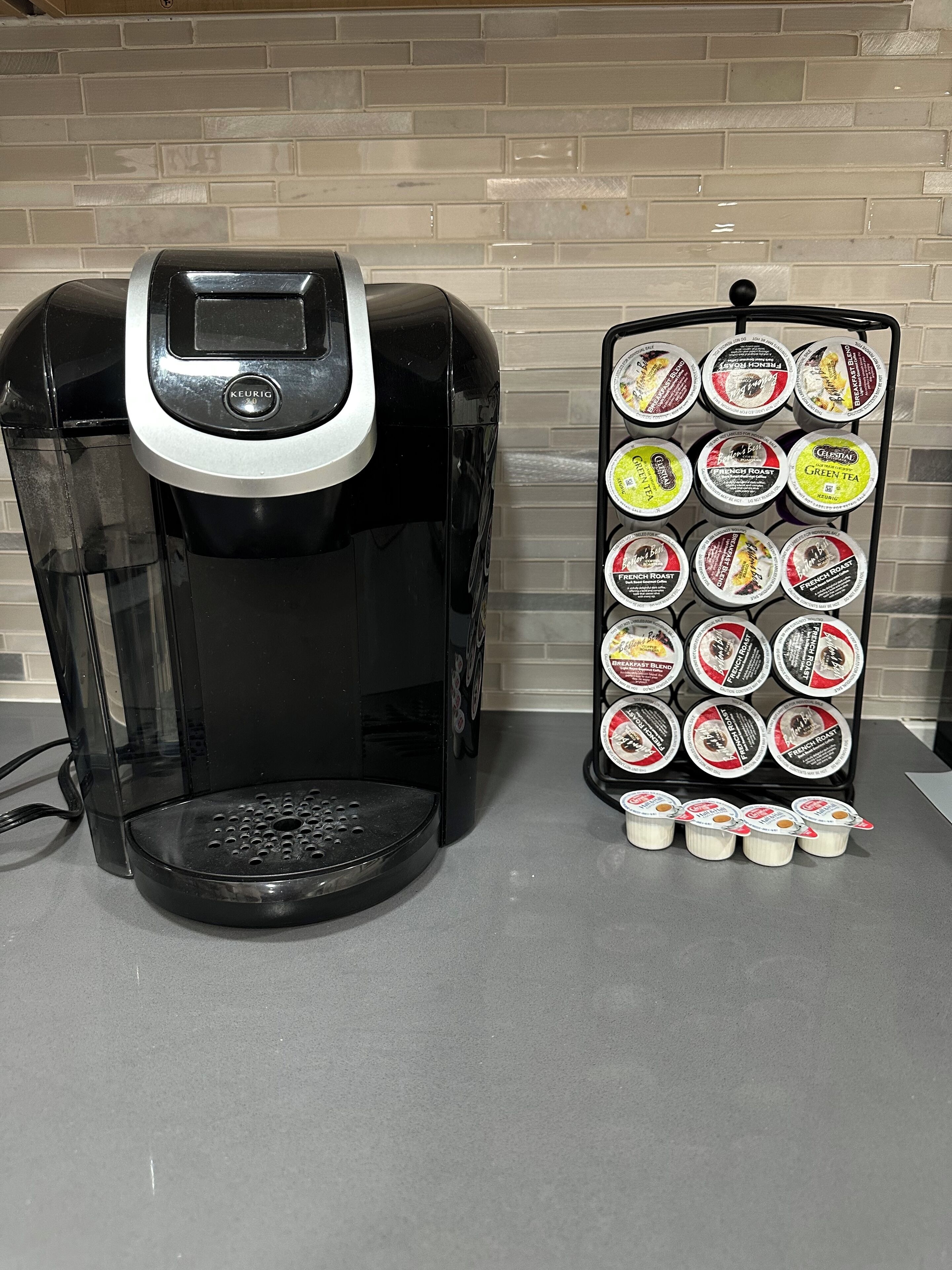 Une machine à café Keurig noire, placée à côté d’un présentoir à dosettes de café de différentes saveurs.
