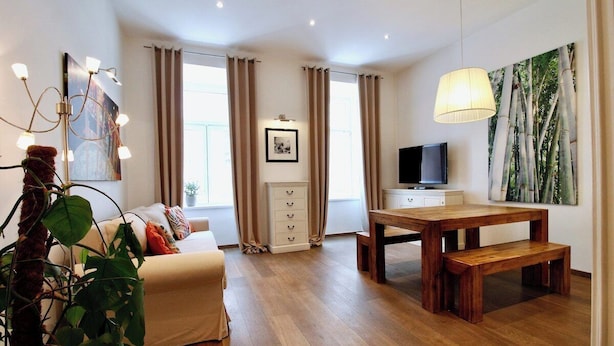 En moderne stue med sofa, et træbord med bænke, et fjernsyn og et stort vindue med gardiner.