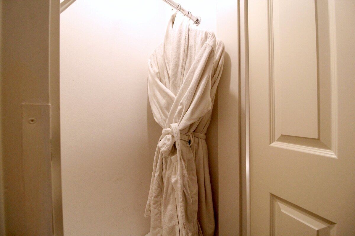 A white robe hanging on a hook in a bathroom with a plain wall and a door with paneling.