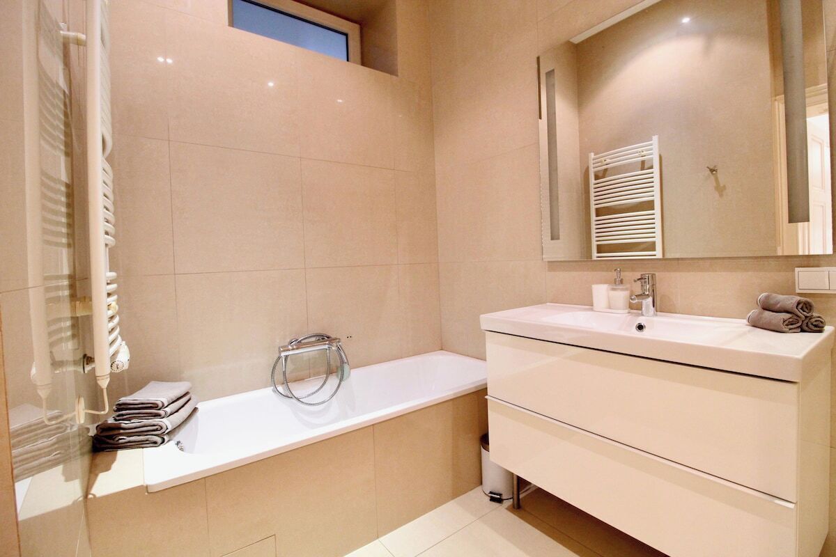 A modern bathroom with a bathtub, a vanity with a mirror, and a towel rack.