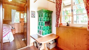 Ein gemütliches Zimmer mit Holzwänden und einem Bett mit floralem Überwurf. Ein grüner Schrank und eine Bank mit Körben darunter sind zu sehen.
