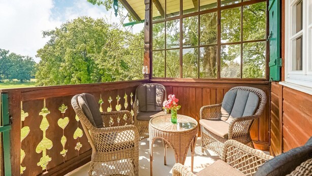 Eine überdachte Veranda mit Korbmöbeln, einem runden Tisch und Blick auf viel Grün.