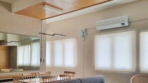 A modern living room with a grey sofa, wooden dining table, and chairs. There is a kitchen area with a stove and cabinets. - Simple & Clutter-Free 2BR, 1BA Condo in Quezon City, near Heart Center & NKTI (Quezon City)