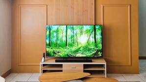 A modern living room with a flat-screen TV mounted on a wooden panel wall, a wooden coffee table, and a gray sofa. - Simple & Clutter-Free 2BR, 1BA Condo in Quezon City, near Heart Center & NKTI (Quezon City)
