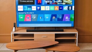 A flat-screen TV on a wooden stand with a remote control and a smartphone on it. - Simple & Clutter-Free 2BR, 1BA Condo in Quezon City, near Heart Center & NKTI (Quezon City)