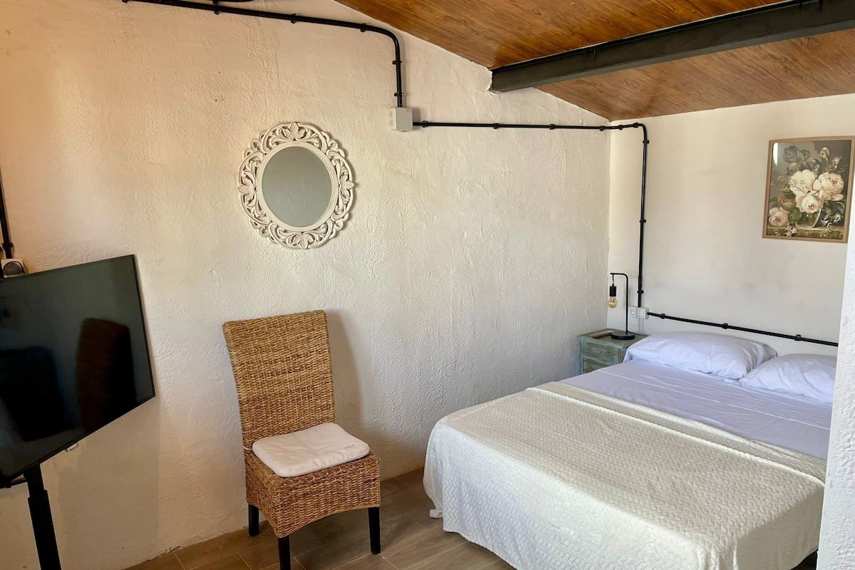 Ein Schlafzimmer mit Bett, Stuhl, Fernseher und einem an der Wand befestigten Spiegel.