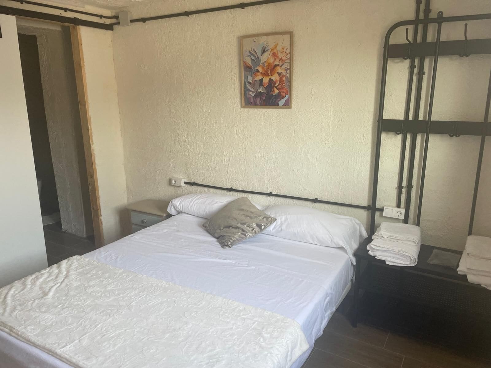 A bedroom with a bed, a nightstand, a painting, and a bunk bed.