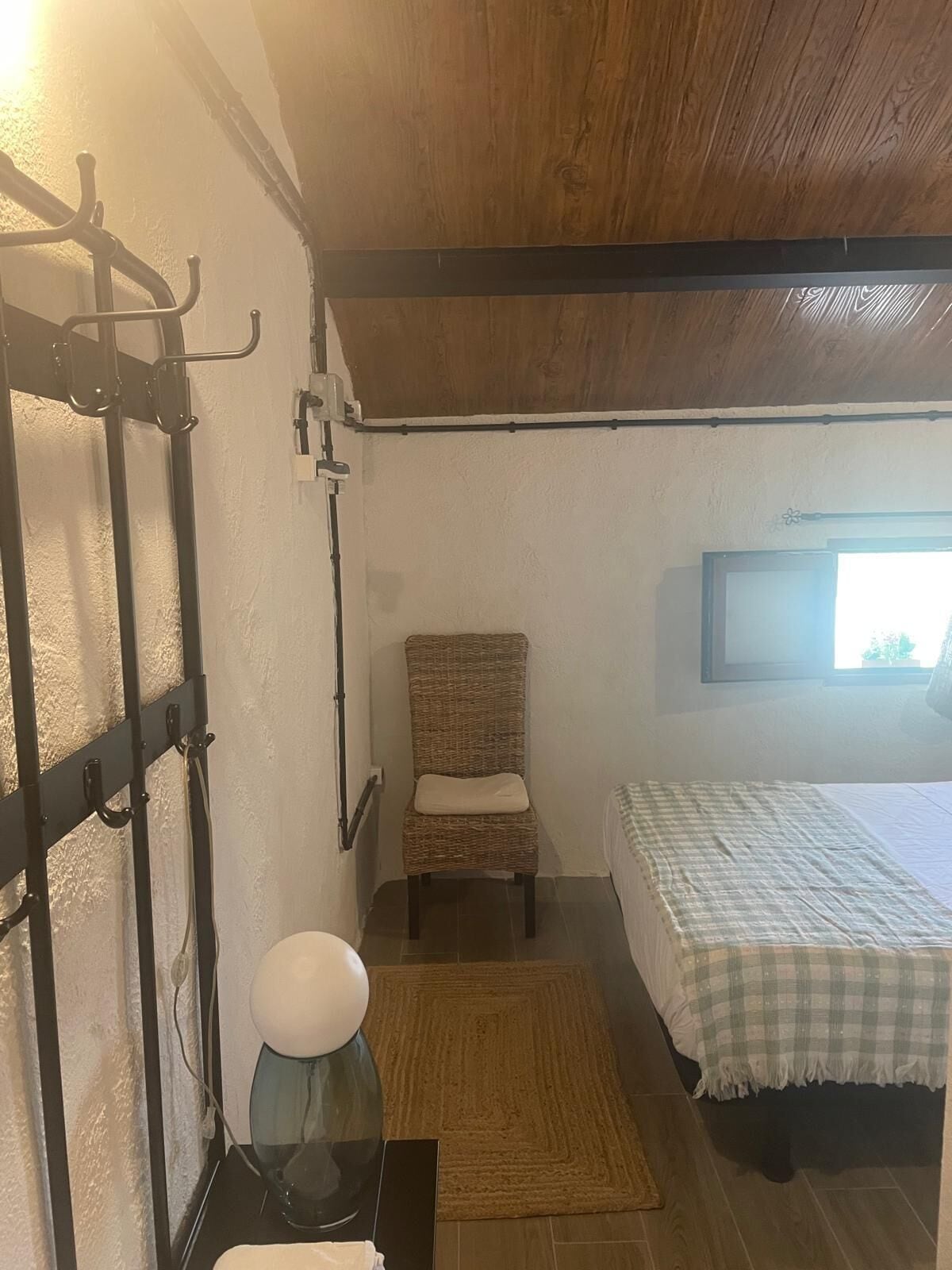 A small, cozy room with a bed, a chair, a wall-mounted TV, and a wooden ceiling.