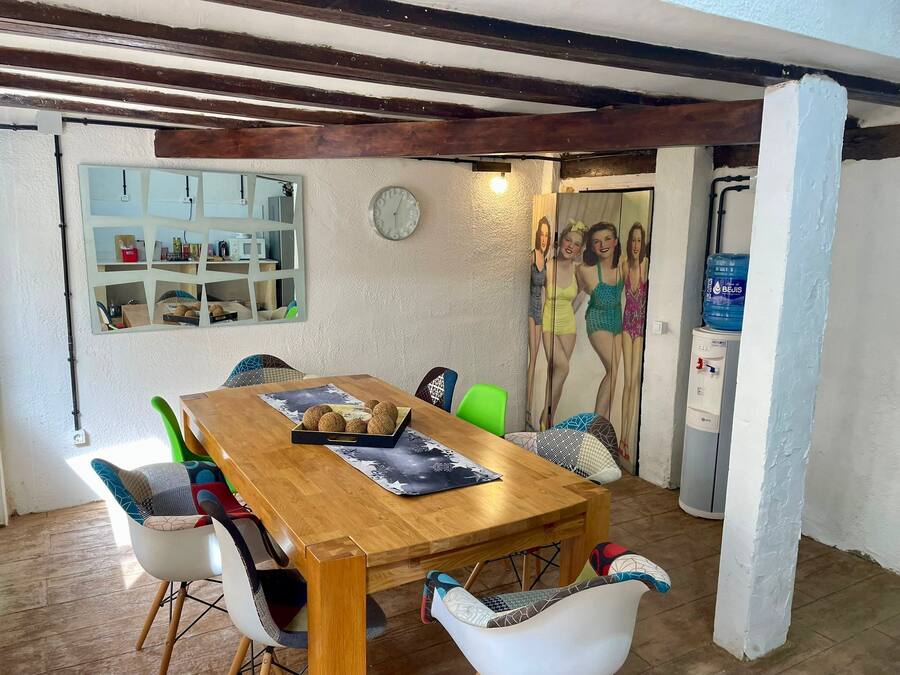 Comedor con mesa de madera, sillas, dispensador de agua y una pared con espejo y reloj.