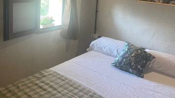 Un dormitorio con cama, ventana con cortinas, un cuadro en la pared y techo de madera.