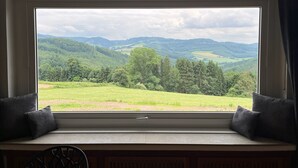 A room with a large window overlooking a green landscape with hills and trees. - Vacation home at Vogelsang (Meschede)